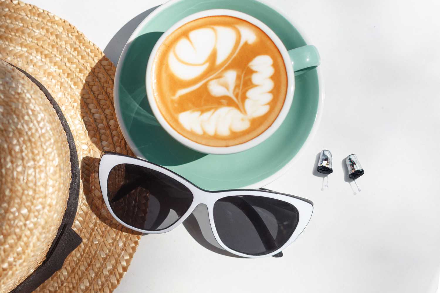 Stilleben mit Strohhut, Tasse Kaffee, Sonnenbrille und zwei Hörgeräten